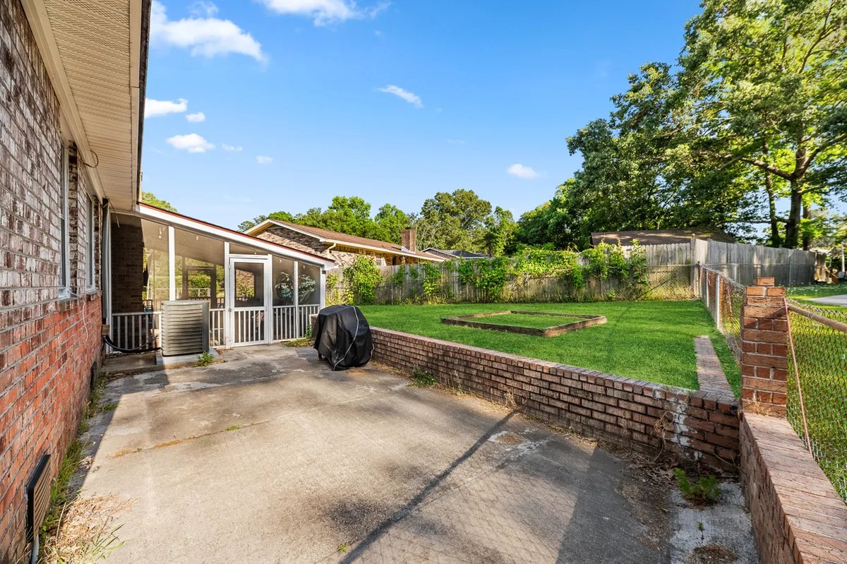 This exterior image showcases a brick wall, a covered grill, a lush green lawn, and mature surrounding trees. The scene hints at outdoor relaxation, casual gatherings, and the peaceful environment surrounding the property.