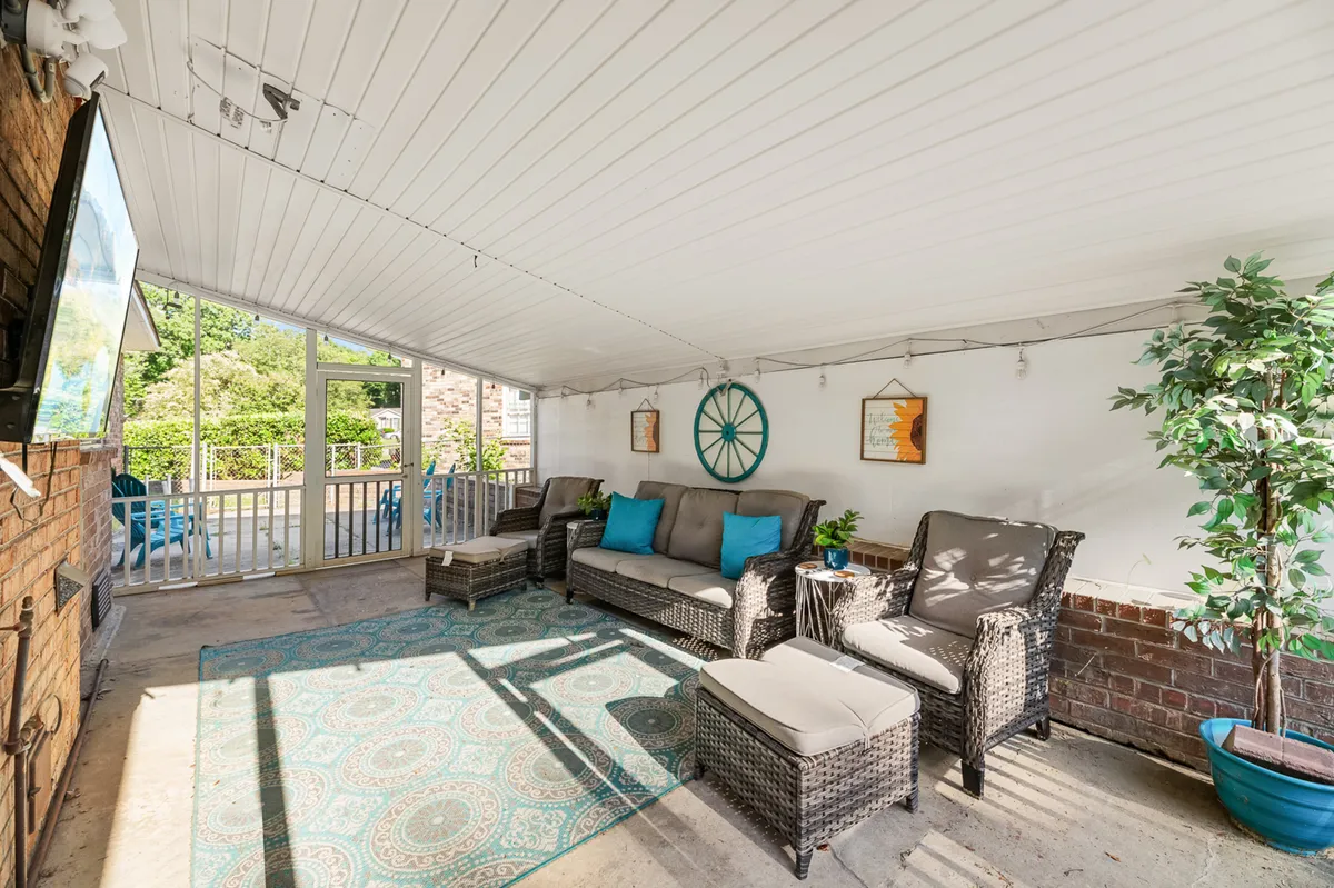A comfortable living area featuring woven furniture, a decorative rug, green plants, wall art, and a television. The mood is cozy and social, suggesting a space equally suited for relaxing, working, or gathering for group activities.