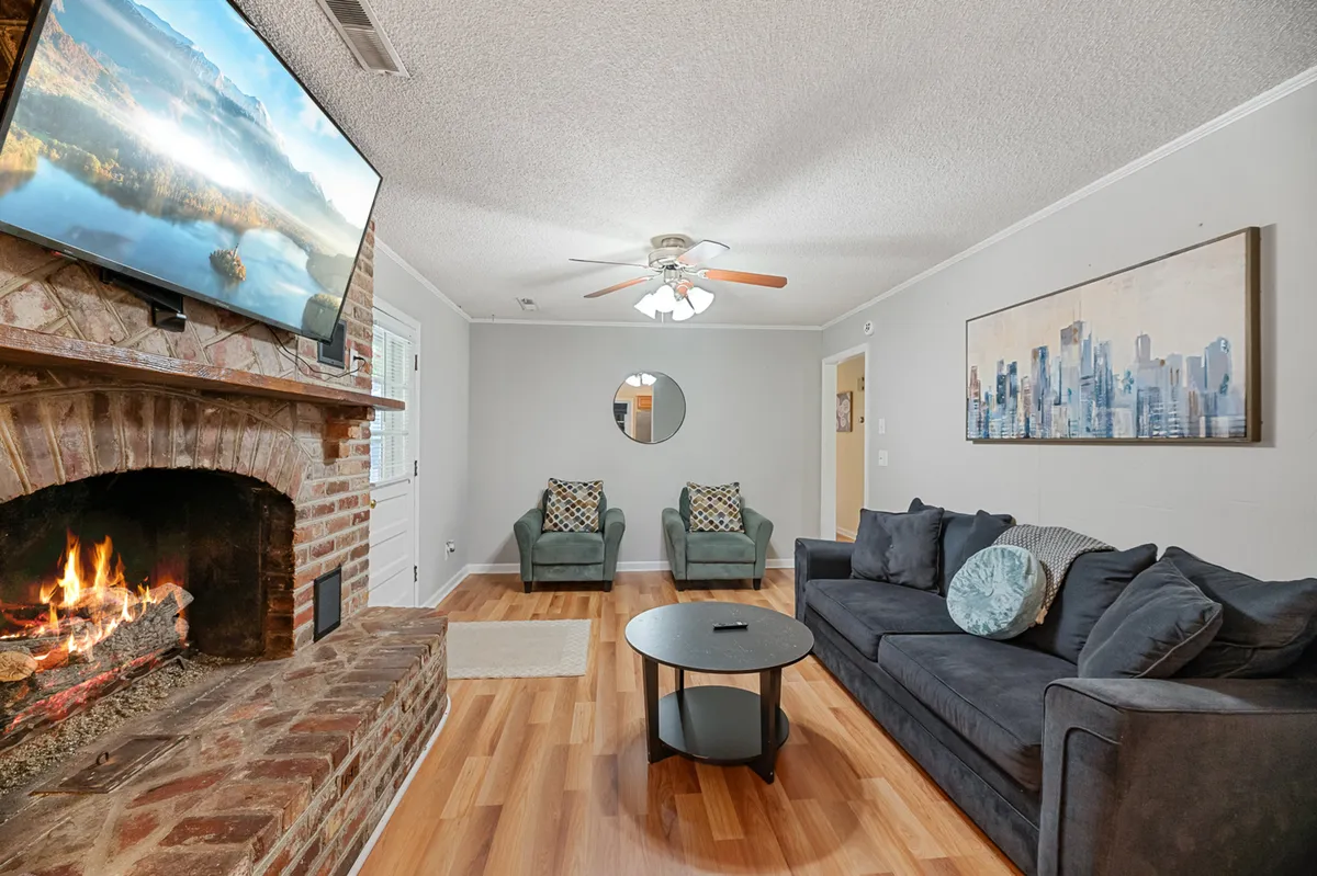 A comfortable living area with a plush sofa, armchairs, a fireplace, and artwork. The arrangement encourages social gatherings, chatting by the fire, or unwinding together for a movie night, all bathed in natural light from nearby windows.