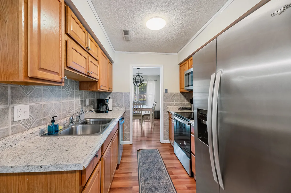 This image showcases a bright and welcoming kitchen featuring granite countertops, stainless steel appliances, warm wood cabinetry, and a functional kitchen island. The space is optimized for both cooking and gathering, with ample counter space and modern amenities evident throughout.