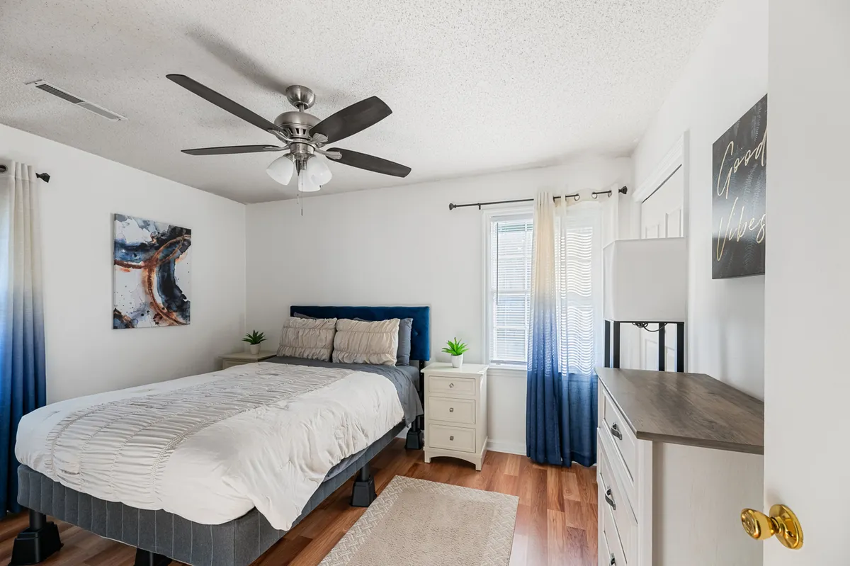 A cozy bedroom scene featuring a bed adorned with decorative pillows, calming wall artwork, and a nightstand with a lamp. The ambiance is soft and tranquil, with subtle natural light enhancing the sense of calm and comfort.