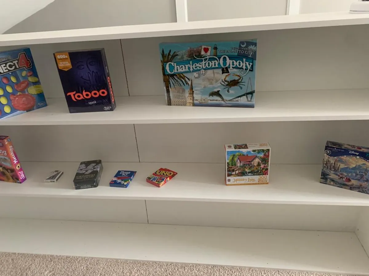 A shelving unit brimming with a variety of board games, set against a backdrop suggesting an area dedicated to friendly competition and group fun. The scene captures the spirit of family game nights and shared entertainment.