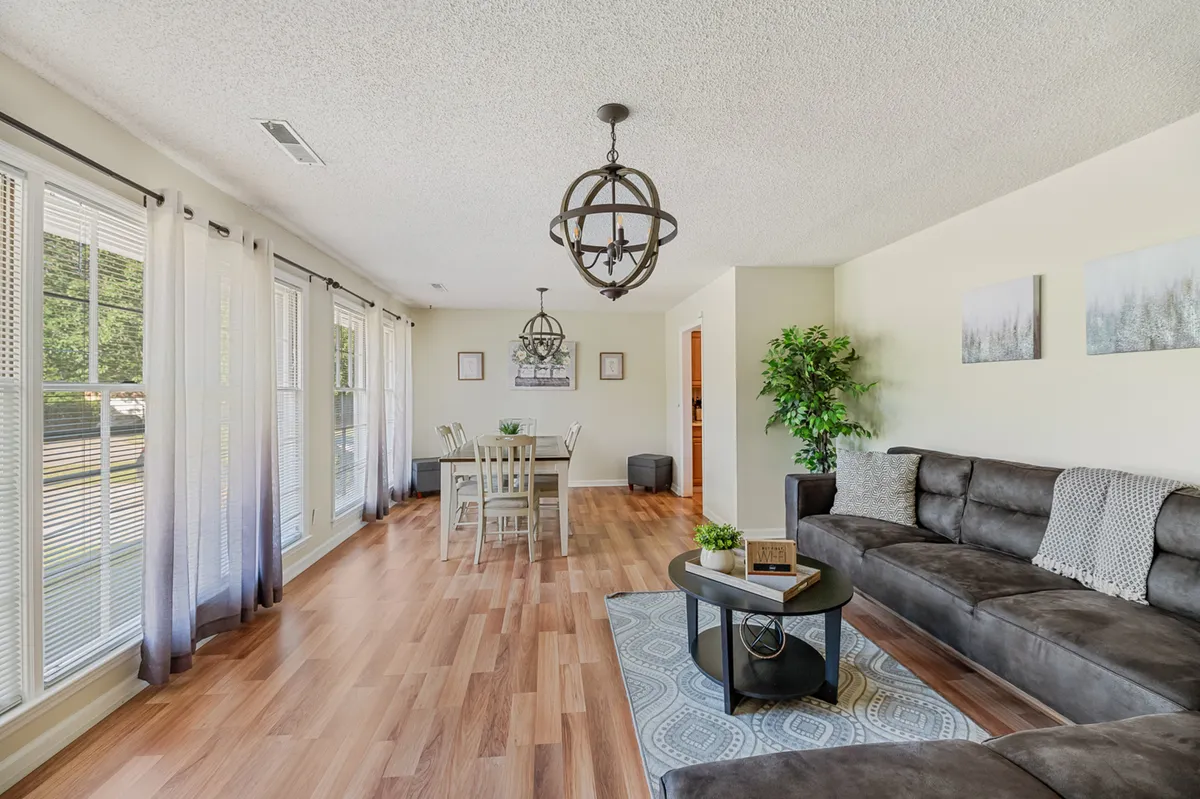A welcoming open-concept space where a sofa and dining table share the same airy, well-lit room. Light fixtures and ample windows create a seamless flow between relaxing and dining areas.
