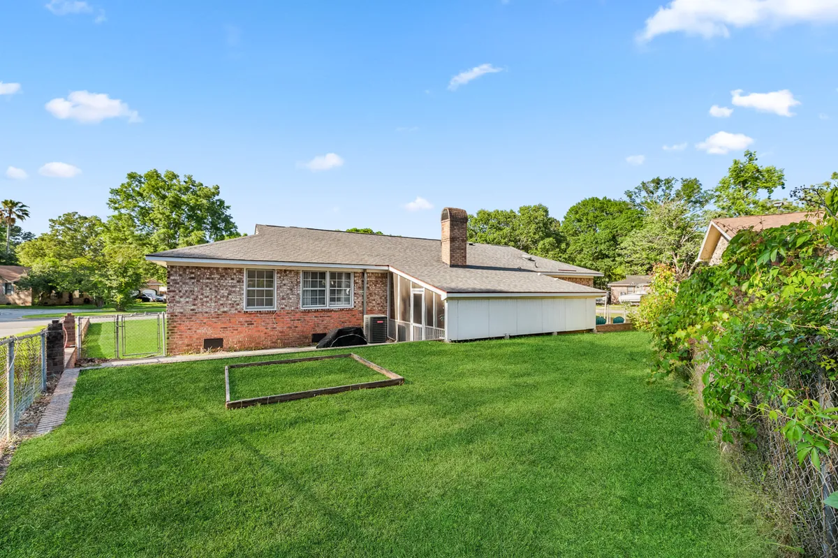 A welcoming view of the brick house with a lush green lawn, tall trees surrounding the property, and a prominent chimney. The open outdoor space hints at ample room for gatherings or games.
