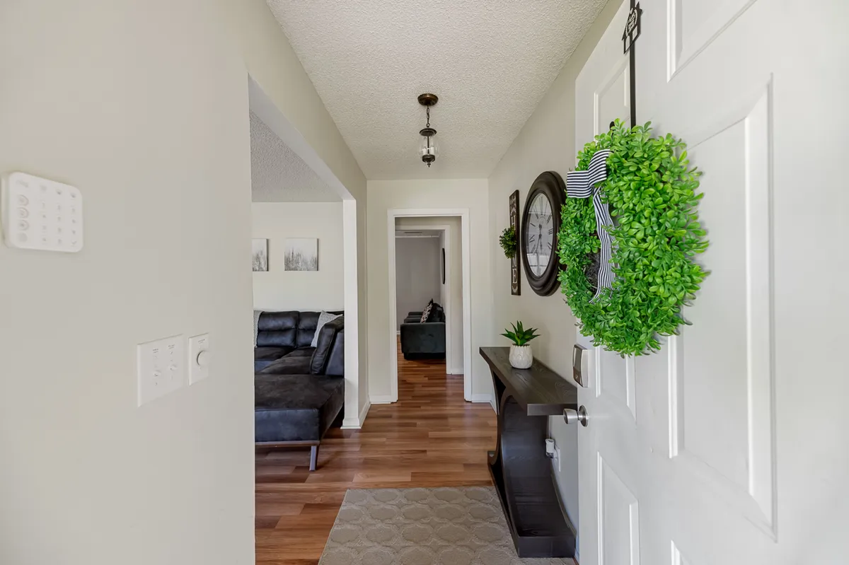 A welcoming view inside the home featuring the front door adorned with a green wreath, a plush sofa, decorative wall clock, and a potted plant. The setup is cozy and inviting, suggesting a comfortable place to return to after work or to host friends and family.