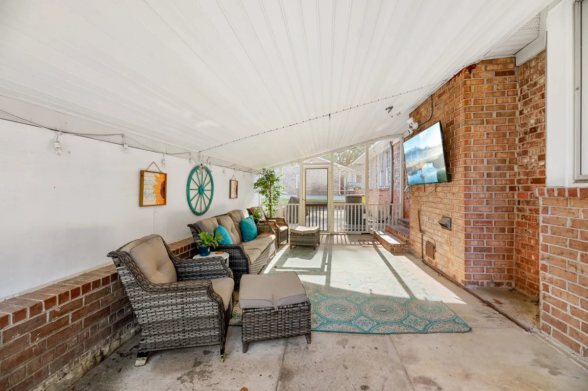 A comfortable indoor setting with wicker seating, decorative wall art, green plants, and a television. The room is bright and appears ideal for relaxing, reading, or enjoying downtime after a workday.